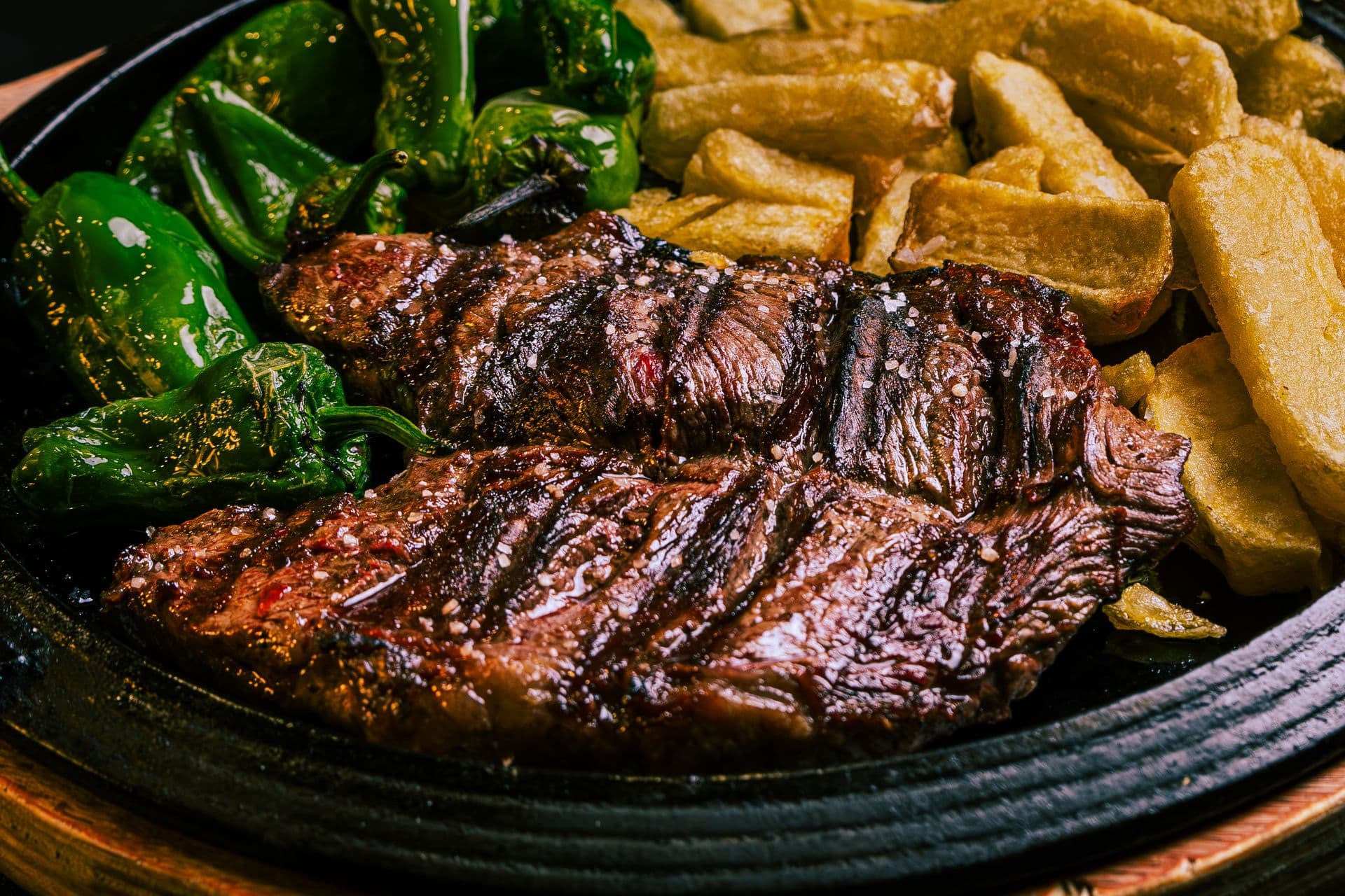 Grilled steak with blistered green peppers and potatoes in a cast-iron dish